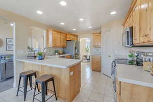 Kitchen with kitchen peninsula, appliances with stainless steel finishes, a kitchen breakfast bar, sink, and light tile patterned flooring