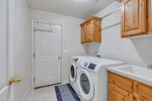 Laundry area featuring cabinets, sink, separate washer and dryer included,  light tile patterned floors