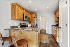 Kitchen featuring sink, dark tile patterned floors, kitchen peninsula, a kitchen bar, and appliances with stainless steel finishes