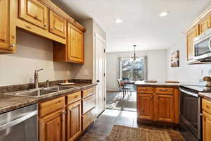 Kitchen with sink, hanging light fixtures, stainless steel appliances, a chandelier, and dark tile patterned flooring