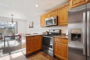 Kitchen with an inviting chandelier, hanging light fixtures, a textured ceiling, appliances with stainless steel finishes, and kitchen peninsula