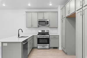 Kitchen with kitchen peninsula, gray cabinetry, stainless steel appliances, sink, and light hardwood / wood-style floors