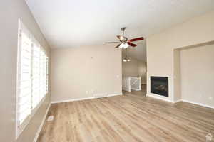 Unfurnished living room featuring a textured ceiling, light hardwood / wood-style floors, vaulted ceiling, and ceiling fan