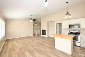 Kitchen featuring appliances with stainless steel finishes, pendant lighting, white cabinetry, a kitchen island, and butcher block counters