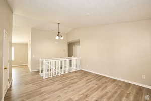 Unfurnished room featuring an inviting chandelier, lofted ceiling, and light wood-type flooring