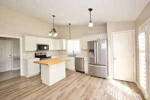 Kitchen featuring appliances with stainless steel finishes, butcher block counters, white cabinets, a kitchen island, and lofted ceiling