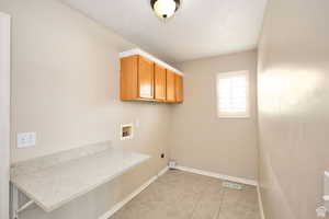 Washroom featuring electric dryer hookup, hookup for a washing machine, light tile patterned floors, and cabinets