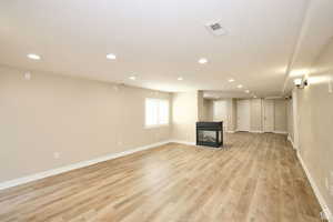 Basement with a multi sided fireplace and light hardwood / wood-style flooring