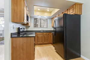 Kitchen with black appliances, a healthy amount of sunlight, a raised ceiling, and light hardwood / wood-style flooring