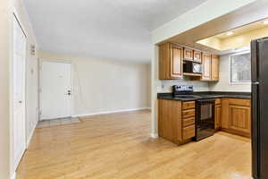 Kitchen with light hardwood / wood-style floors, ornamental molding, and black appliances