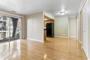 Unfurnished living room with a textured ceiling, light wood-type flooring, and crown molding