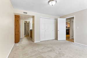 Unfurnished bedroom featuring ensuite bathroom, a closet, light colored carpet, and a textured ceiling