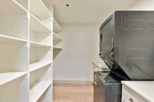 Laundry room with stacked washer / drying machine and light hardwood / wood-style flooring