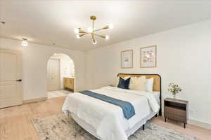 Bedroom with ensuite bathroom, wood-type flooring, and an inviting chandelier