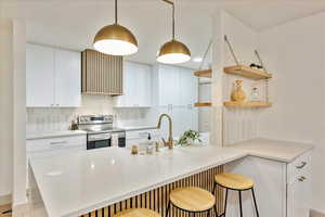 Kitchen with hanging light fixtures, a kitchen breakfast bar, stainless steel electric range, decorative backsplash, and white cabinets