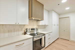 Kitchen with white cabinetry, tasteful backsplash, range hood, stainless steel range with electric cooktop, and light wood-type flooring