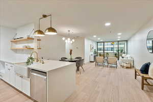 Kitchen with sink, dishwasher, hanging light fixtures, light hardwood / wood-style flooring, and white cabinets