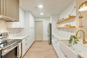 Kitchen with white cabinets, light wood-type flooring, backsplash, and appliances with stainless steel finishes