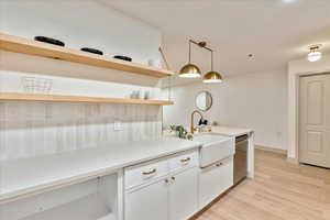 Kitchen featuring pendant lighting, white cabinets, sink, stainless steel dishwasher, and light hardwood / wood-style floors