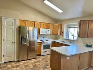 Kitchen featuring lofted ceiling, white appliances, sink, and kitchen peninsula