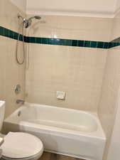 Bathroom with hardwood / wood-style floors, tiled shower / bath combo, and toilet