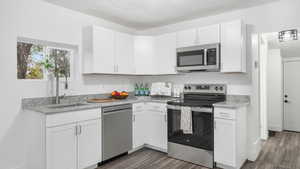 Kitchen featuring white cabinets, sink, dark hardwood / wood-style floors, light stone countertops, and stainless steel appliances