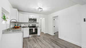 Kitchen with white cabinetry, sink, stainless steel appliances, and light hardwood / wood-style floors