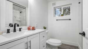 Bathroom featuring hardwood / wood-style flooring, vanity, toilet, and a tile shower