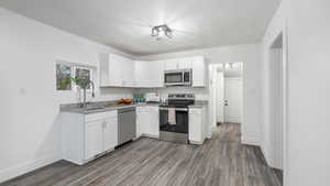 Kitchen with sink, light hardwood / wood-style flooring, a textured ceiling, white cabinets, and appliances with stainless steel finishes