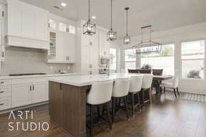 Kitchen with appliances with stainless steel finishes, dark hardwood / wood-style flooring, a breakfast bar, a kitchen island with sink, and white cabinets