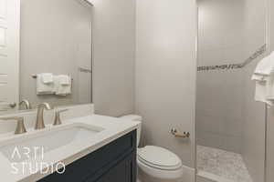 Bathroom featuring a tile shower, vanity, and toilet