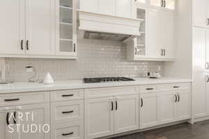 Kitchen with custom exhaust hood, stainless steel gas stovetop, white cabinets, decorative backsplash, and dark hardwood / wood-style flooring