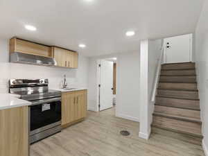 Kitchen featuring stainless steel range with electric stovetop, light brown cabinets, sink, wall chimney exhaust hood, and light hardwood / wood-style floors