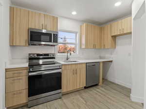 Kitchen with sink, light hardwood / wood-style flooring, light brown cabinets, and appliances with stainless steel finishes