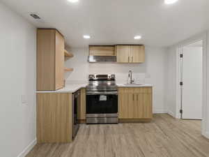 Kitchen with light brown cabinetry, light wood-type flooring, ventilation hood, sink, and stainless steel range with electric cooktop