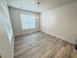 Unfurnished dining area featuring light hardwood / wood-style floors, a textured ceiling, and an inviting chandelier