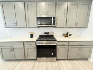 Kitchen with decorative backsplash, appliances with stainless steel finishes, light wood-type flooring, and gray cabinets