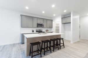 Kitchen featuring light wood-type flooring, backsplash, gray cabinetry, stainless steel appliances, and a center island with sink