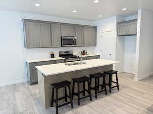 Kitchen featuring gray cabinetry, a center island with sink, sink, light wood-type flooring, and appliances with stainless steel finishes