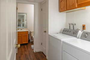 Clothes washing area featuring cabinets, sink, washer and dryer, and dark hardwood / wood-style floors