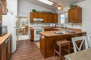 Kitchen with sink, white appliances, kitchen peninsula, and dark wood-type flooring