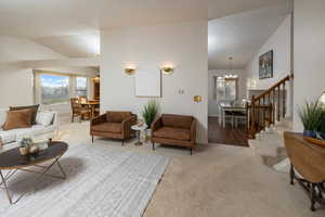 Living room featuring carpet flooring, vaulted ceiling, and an inviting chandelier