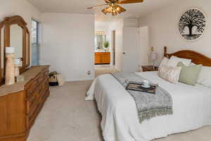 Bedroom with connected bathroom, light colored carpet, and ceiling fan