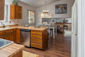 Kitchen with sink, hanging light fixtures, a brick fireplace, stainless steel dishwasher, and white refrigerator