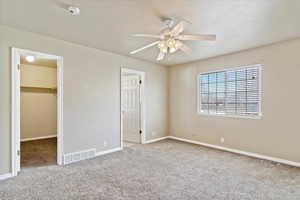 Primary bedroom with a walk in closet, ceiling fan, a closet, and carpet