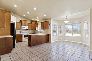 Kitchen featuring kitchen peninsula,  appliances, hanging light fixtures, lofted ceiling, and light tile patterned flooring