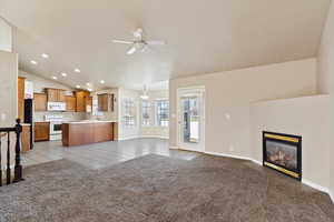 Unfurnished living room featuring light carpet, vaulted ceiling, and ceiling fan