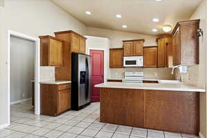 Kitchen featuring sink, kitchen peninsula, vaulted ceiling, appliances, and light tile patterned floors