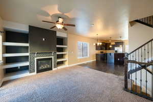 Living room with a fireplace, dark hardwood / wood-style flooring, built in features, and ceiling fan with notable chandelier