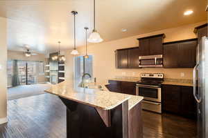 Kitchen featuring appliances with stainless steel finishes, a breakfast bar, ceiling fan with notable chandelier, sink, and hanging light fixtures